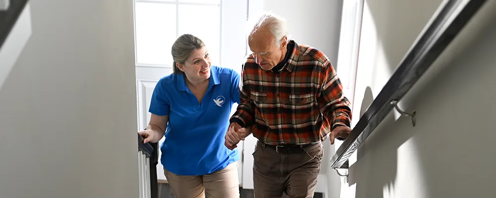 Visiting Angels caregiver assisting an elderly man up the stairs.