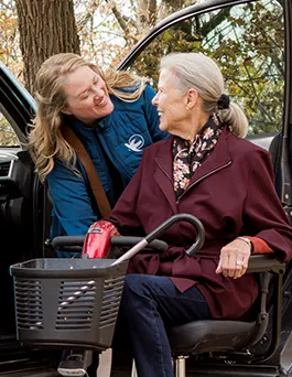 A female Visiting Angels senior home care provider helps an elderly woman into her car.