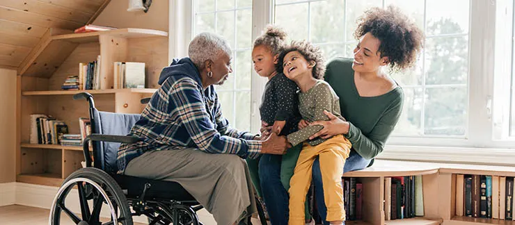Family caregiver spending quality time with an older loved one in a wheelchair and two young children at home.