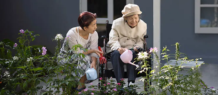 Female caregiver helping senior woman water plants in the garden.