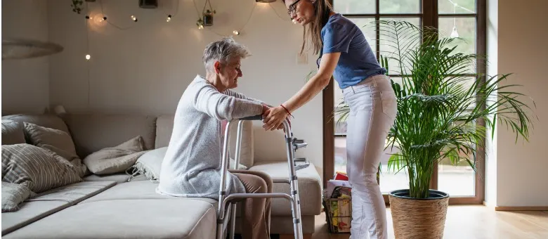 A caregiver helping an elderly woman stand up. They are using a walker for support.